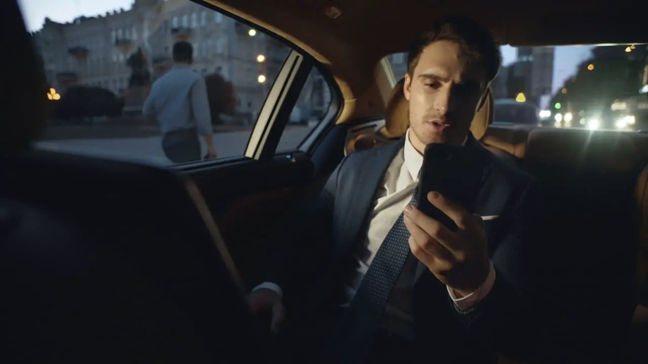 Tired male professional speaking on video call on smartphone in dark luxury car