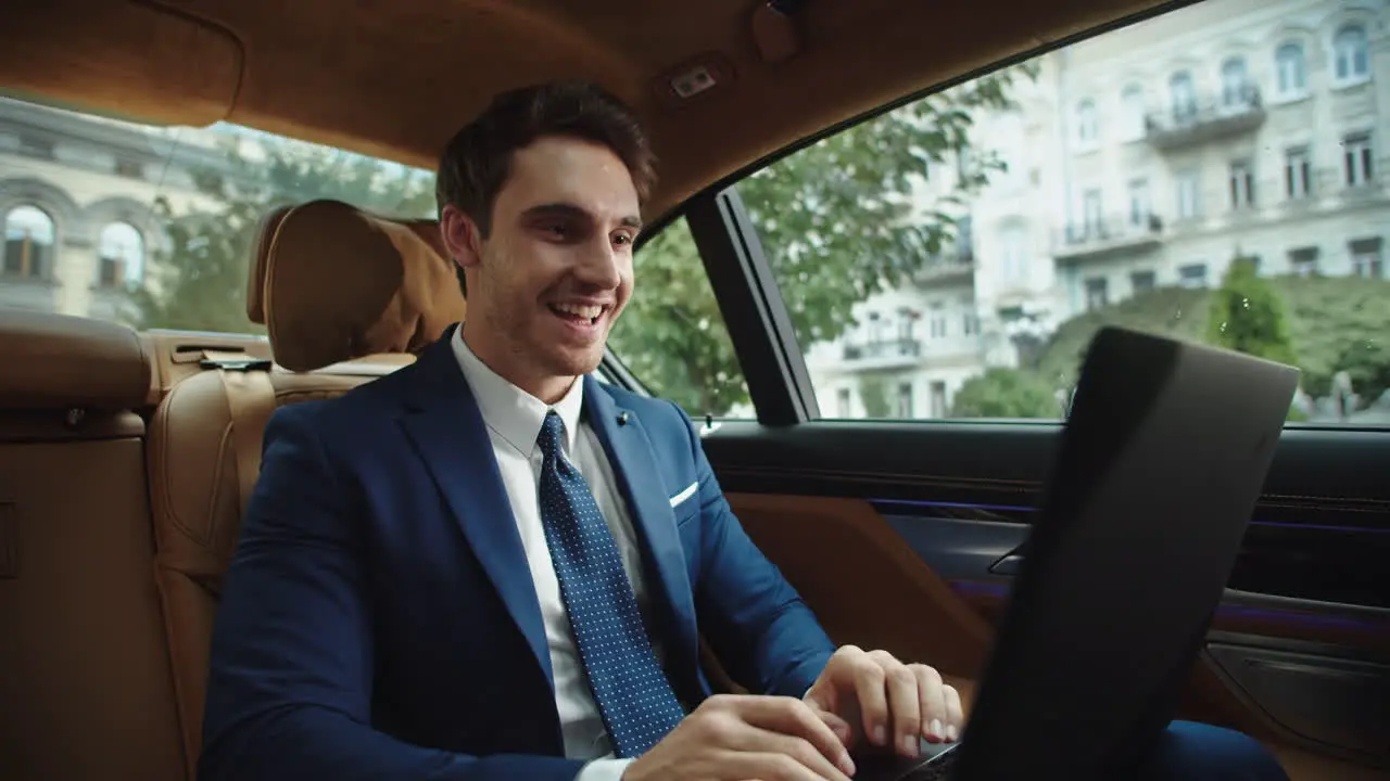 Cheerful businessman typing laptop in luxury car Male ceo celebrating success