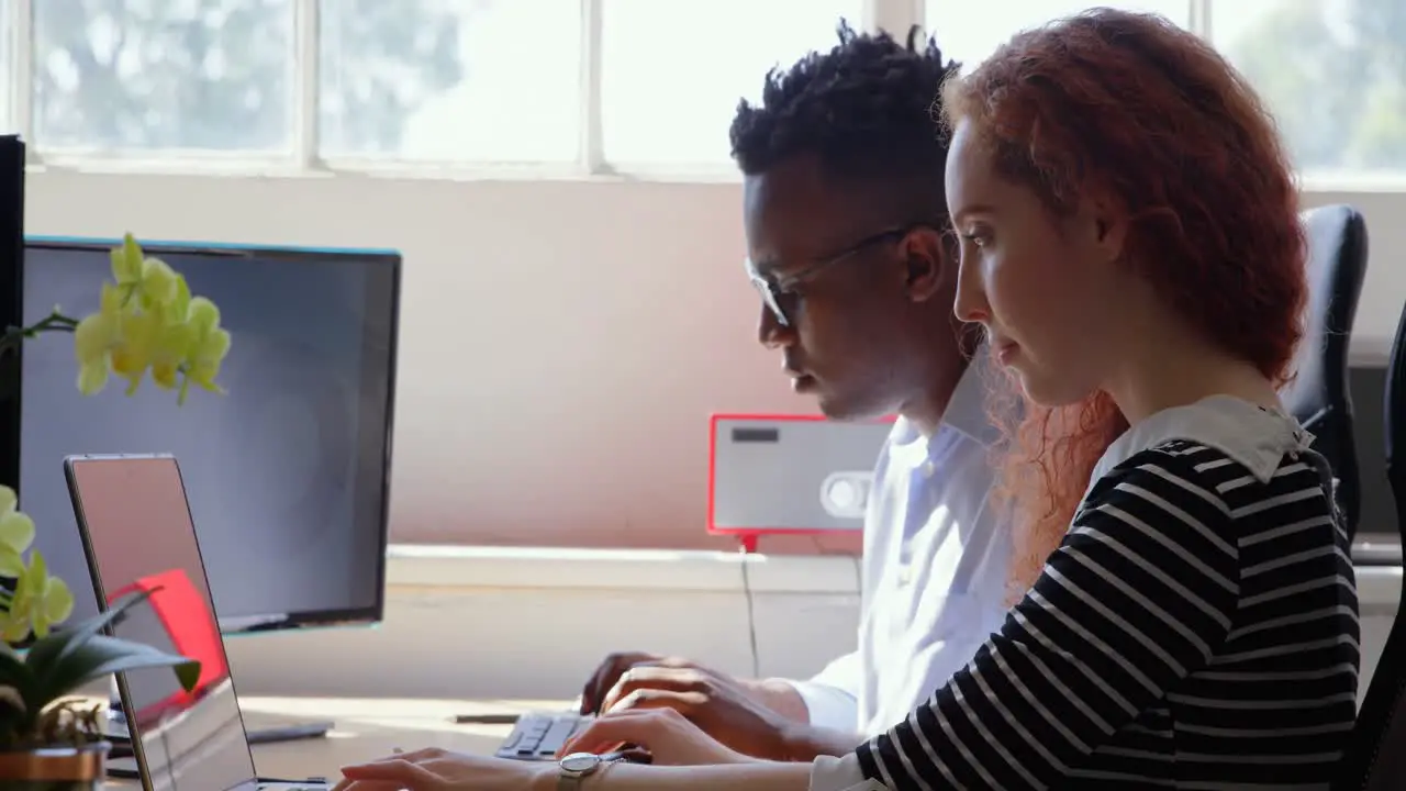 Side view of young mixed-race business team working on laptop and desktop pc in a modern office 4k