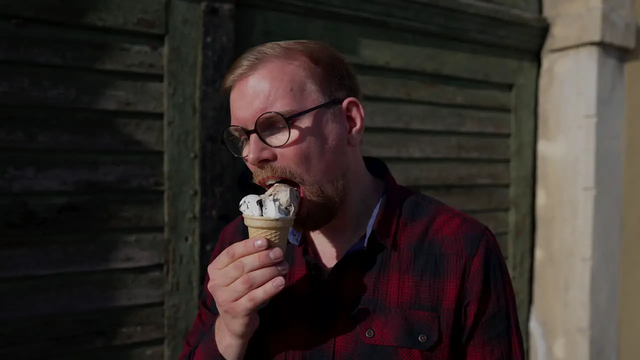 Young Man with Glasses Eats Ice Cream in Cone Sunny Day Outside