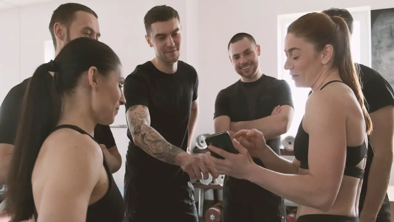 Strong Young Woman Shows Something To Her Gym Buddies On Her Mobile Phone