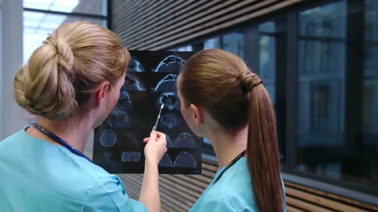 Two nurses examining an x-ray report in corridor