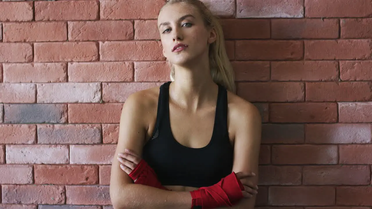 Positive sportswoman leaning on brick wall