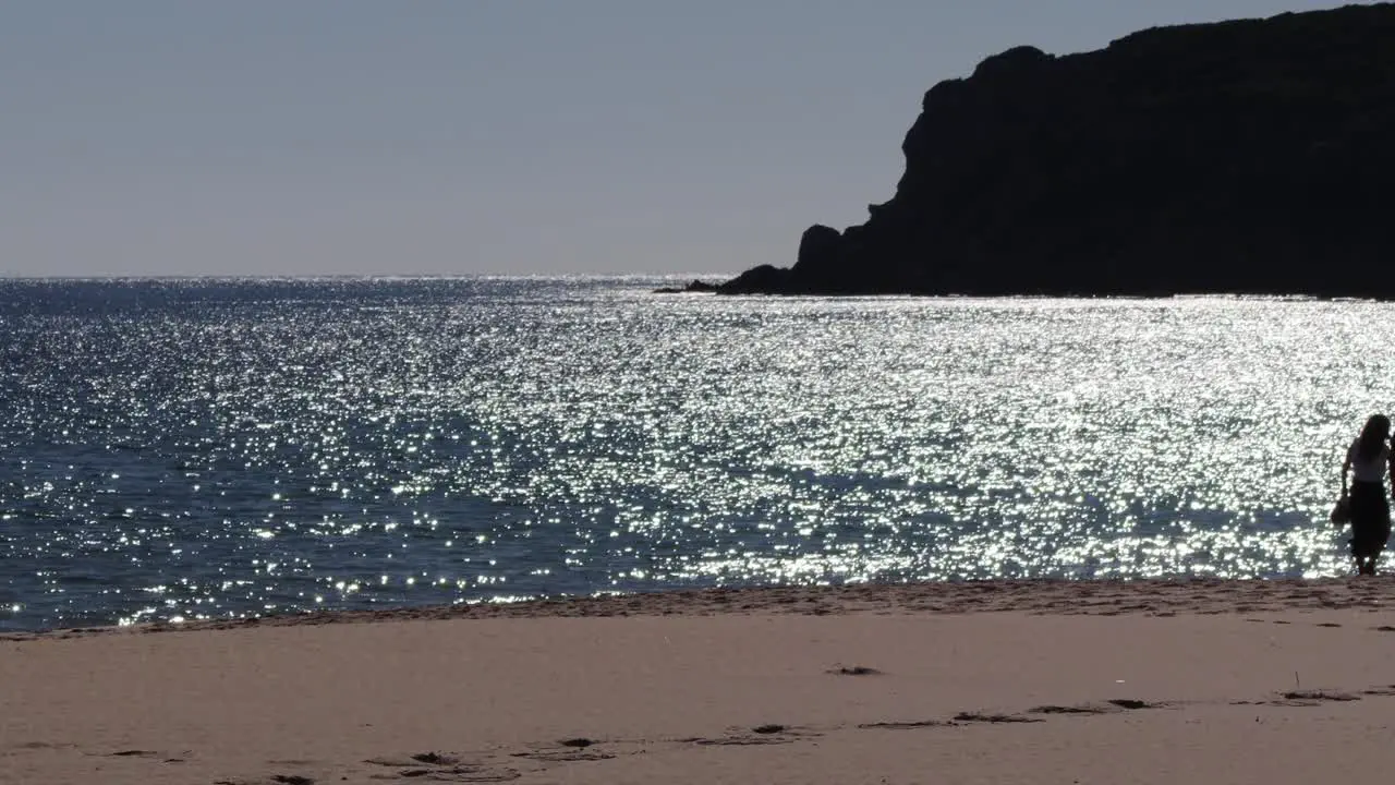 Cinematic Scene of People Silhouettes Strolling the Beach with Glittering Ocean on the Background