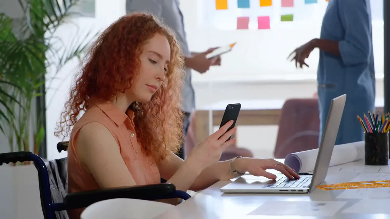 Side view of disable young caucasian businesswoman working on laptop and smartphone in office 4k