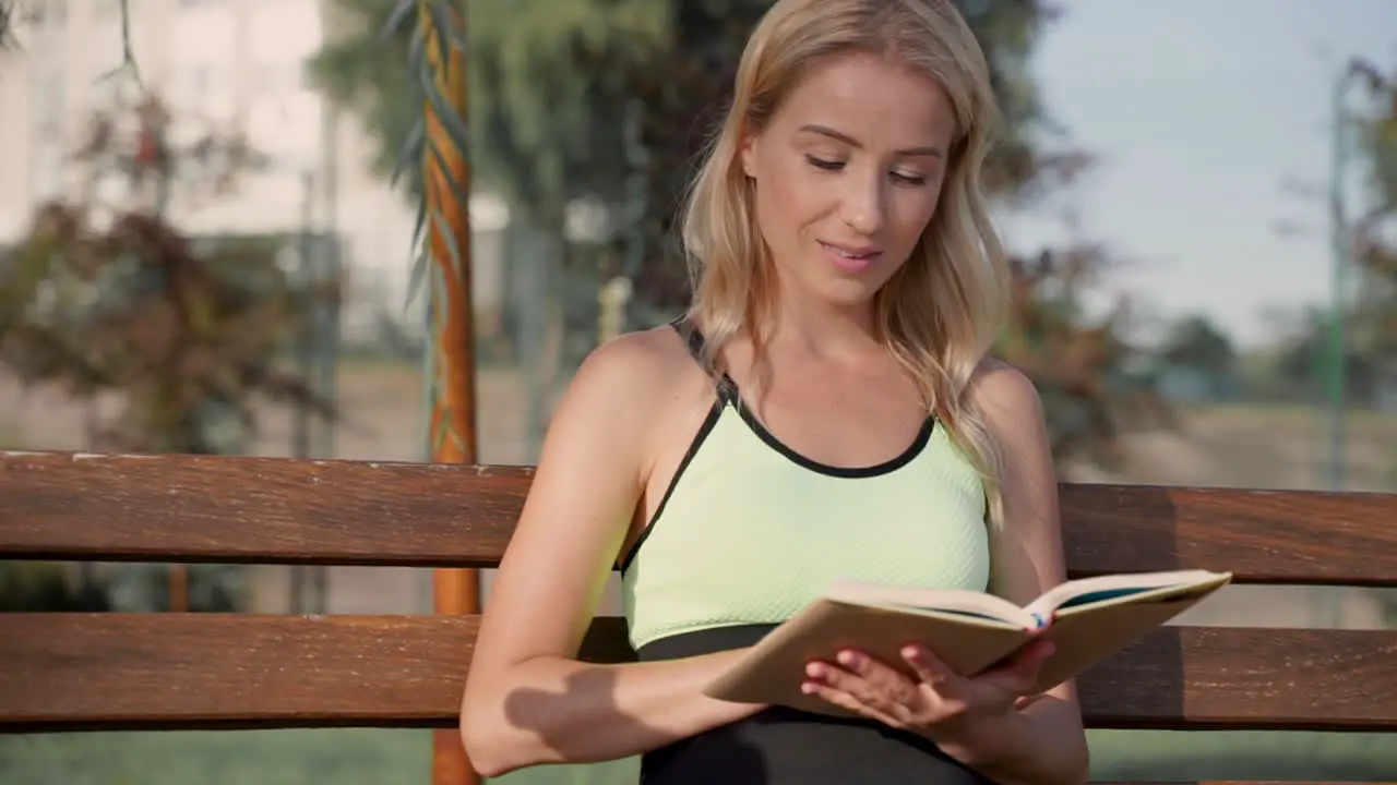 Happy Athlete Woman Enjoying Reading A Book Sitting On A Bench Outdoors