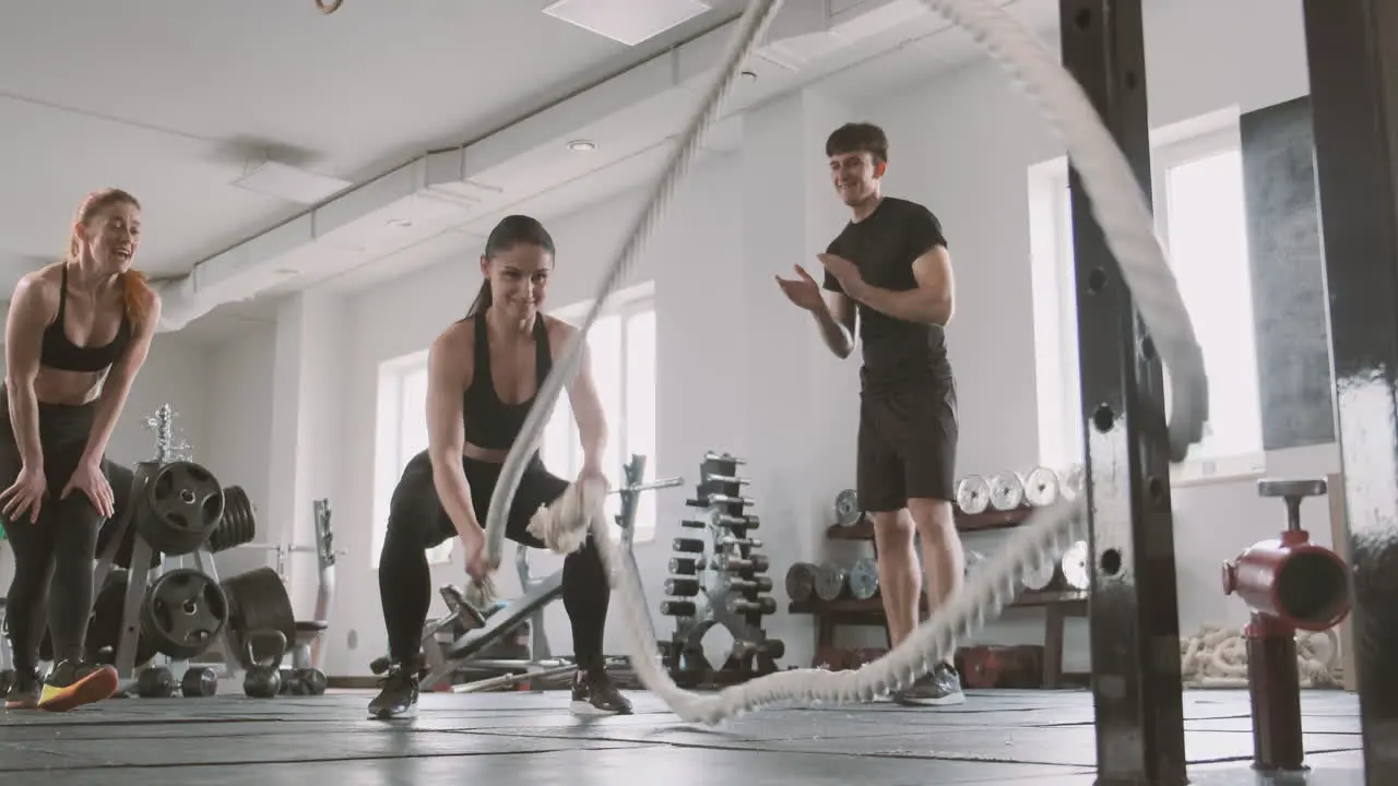 An Athletic Woman Works With Battling Ropes While Gym Buddies Support Her