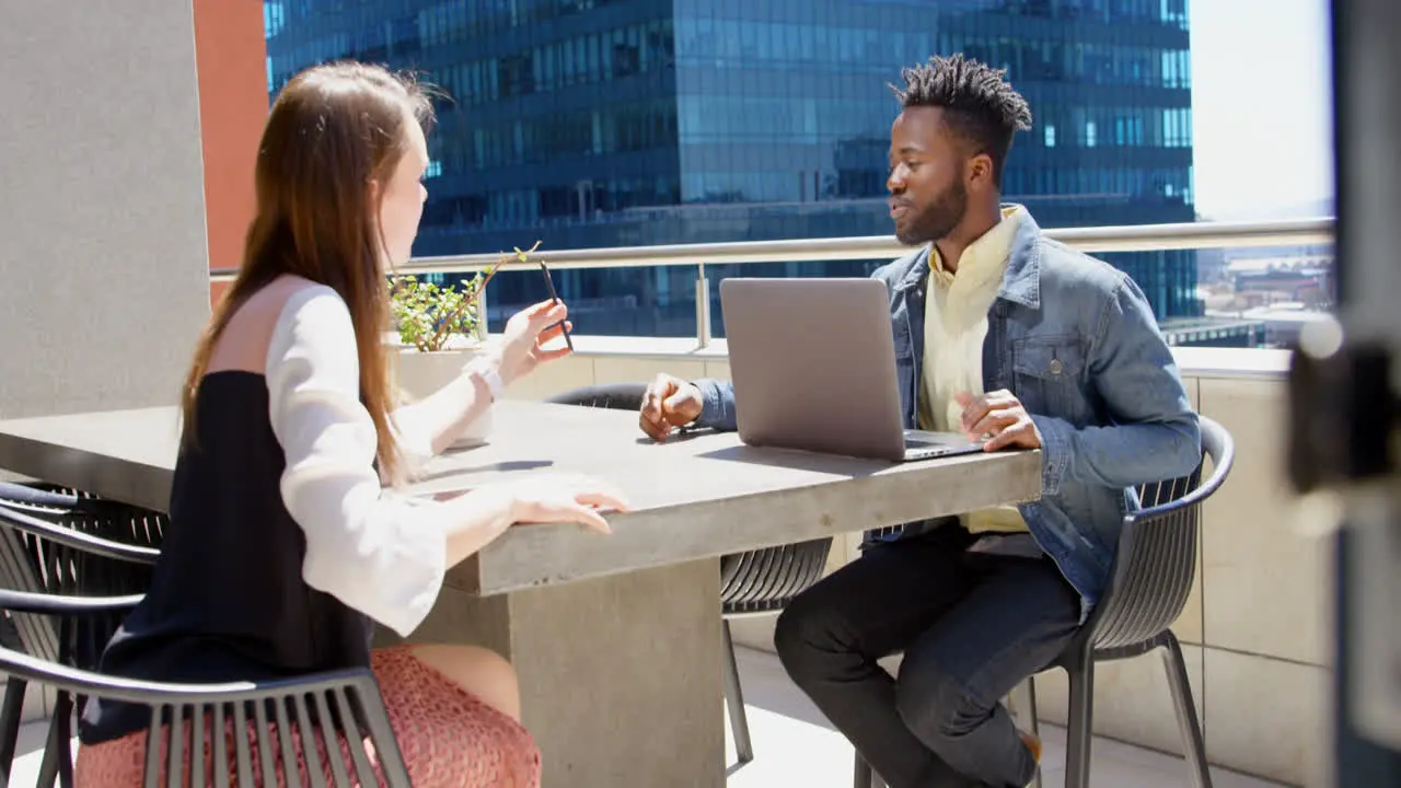 Side view of young mixed-race business team planning and sitting at table in office balcony 4k