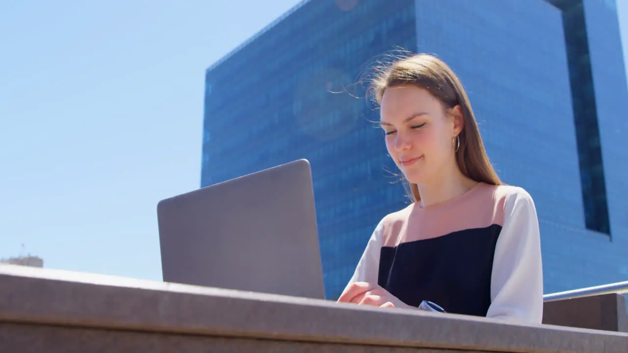 Front view of young cool caucasian businesswoman working on laptop in balcony of modern office 4k