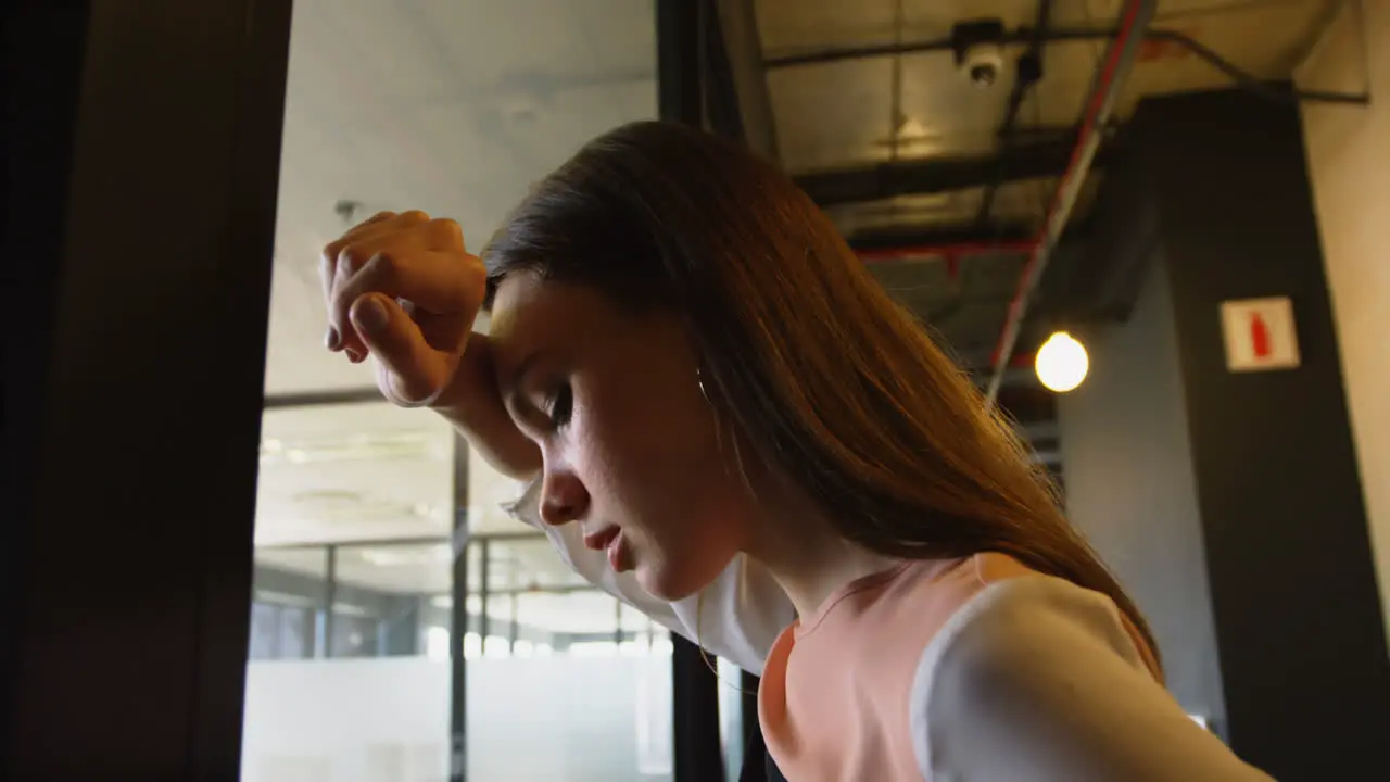 Low angle side view of young Caucasian businesswoman leaning head against glass wall in modern offic