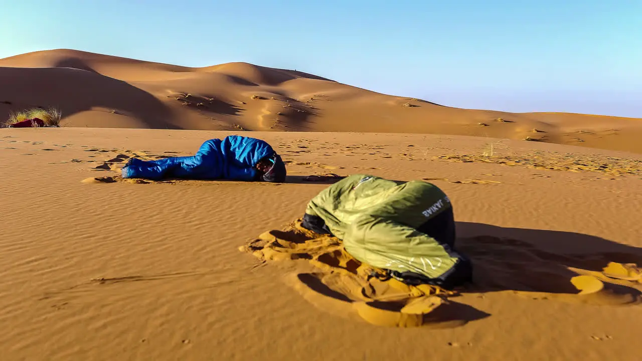 Two people sleeping in sleeping bags in the desert