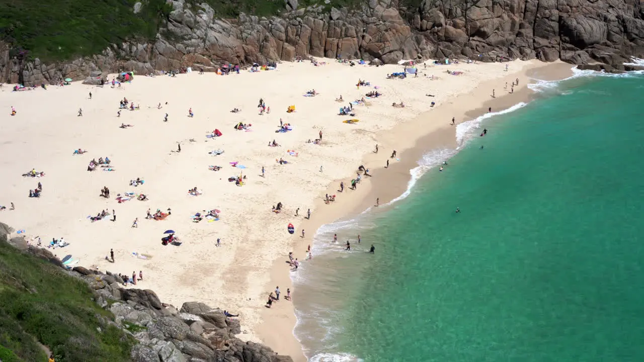 Aerial view of Porthcurno Beach in Cornwall full of tourists swimmers surfers and families having fun on a beautiful spring sunny day