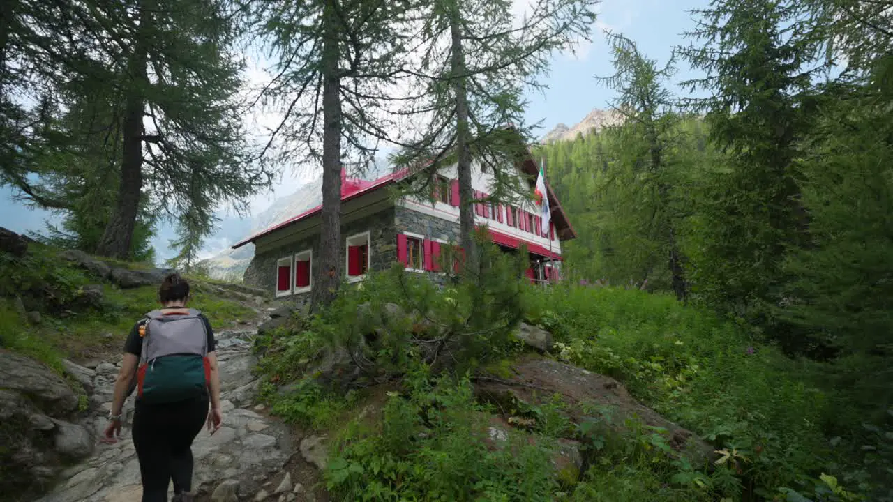 Woman trekking in summer season toward red colored mountain refuge of Alpe Ventina in Valmalenco Italy