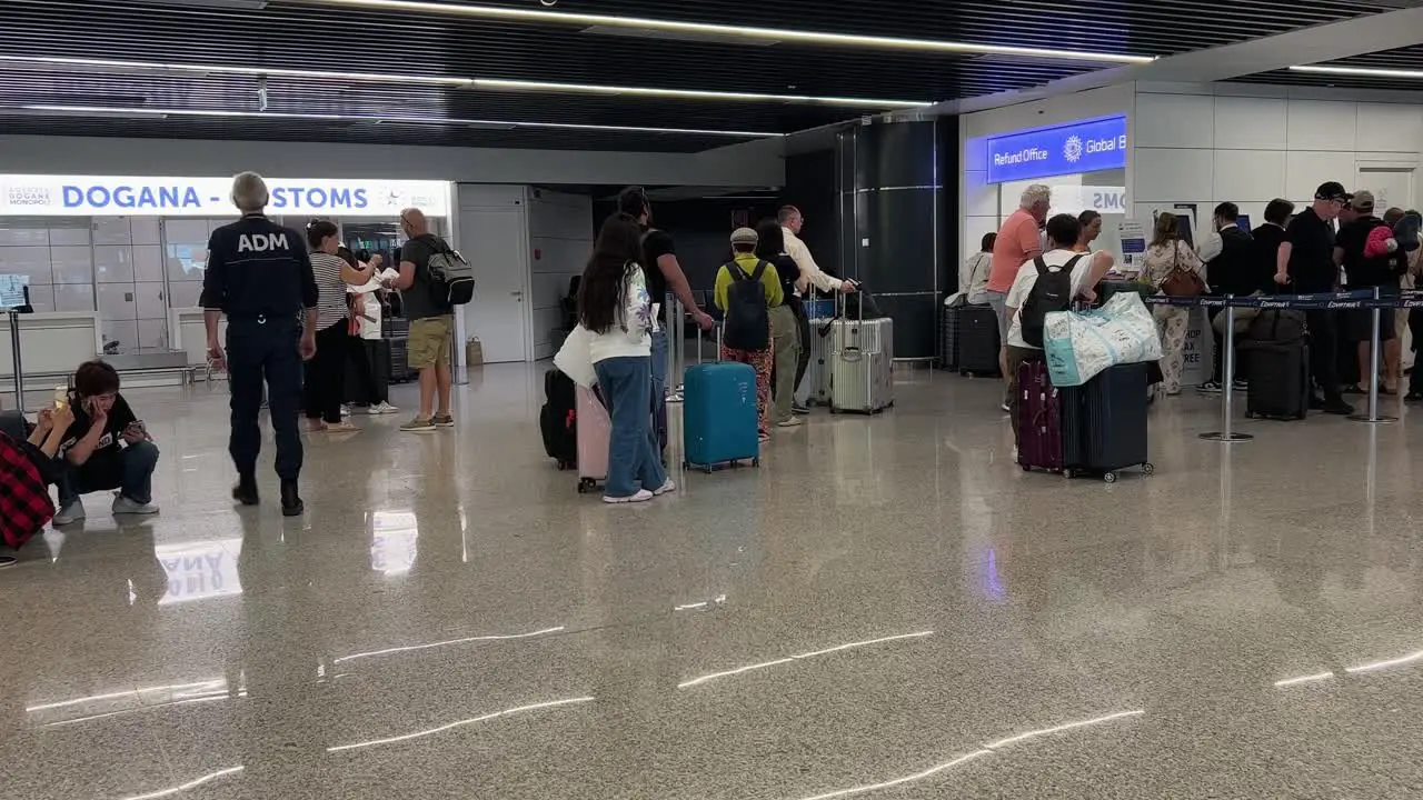 Customs officer walks toward customs office inside airport as line of people wait their turn at tax refund front desk