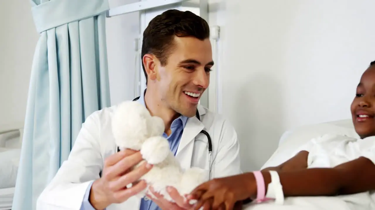 Doctor entertaining sick boy with teddy bear