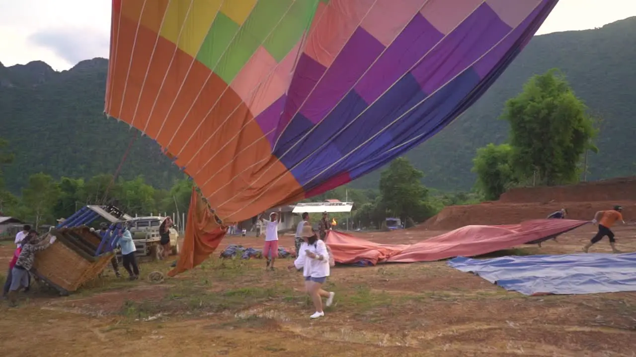 A hot air balloon have landed and the balloon slowly sinks down to the ground as people are wokring to get it in the right direction