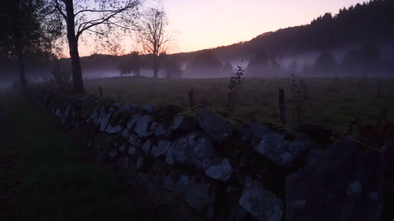 camera follow a stone wall in the nature with a misty field in the background