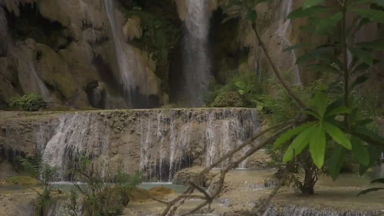 slow motion clip on a small waterfall with green leafs in front of the camera