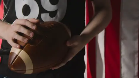 Close Up Of American Football Player Holding Ball Against Stars And Stripes Flag In Background