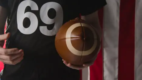 Close Up Of American Football Player Holding Ball Against Stars And Stripes Flag In Background 1