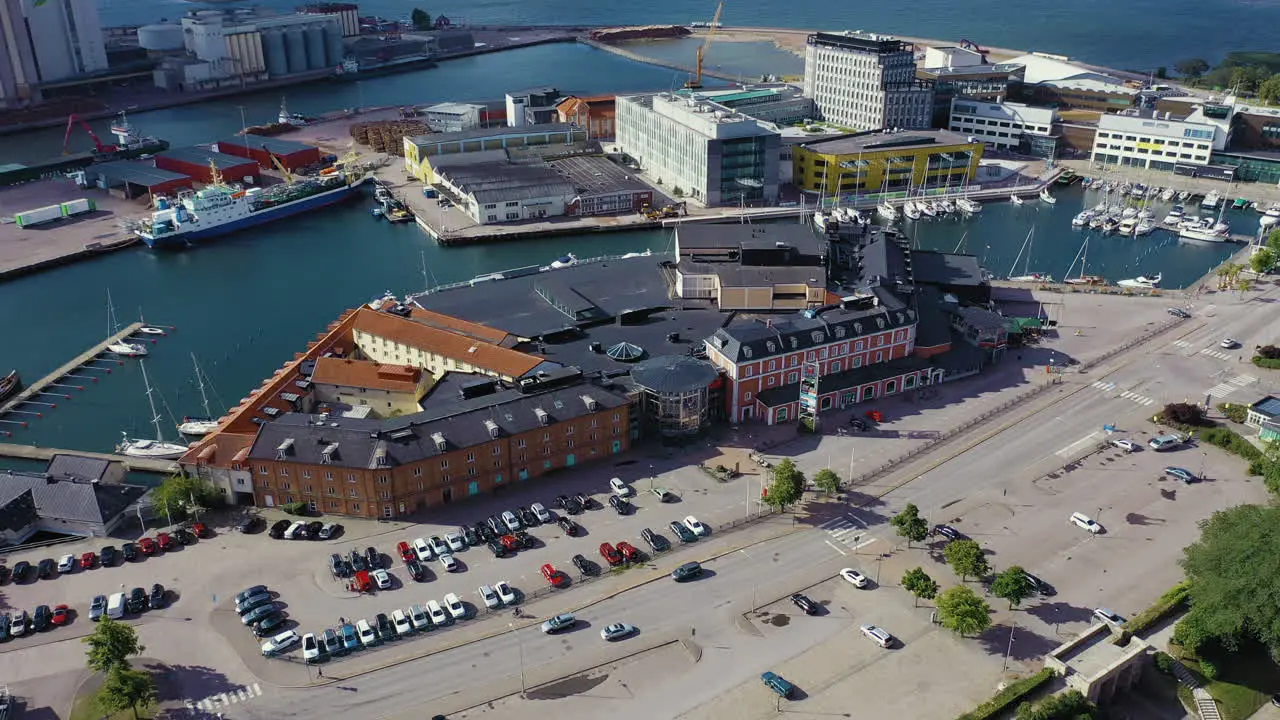 Camera pans away from shopping mall near seaside boat docks with large parking lot in European city tourists attraction visiting Denmark brick building aerial drone sunny day hot stores car vfx 3D