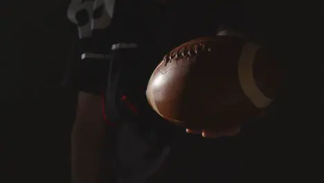 Close Up Studio Shot Of American Football Player Holding Out Ball With Low Key Lighting 