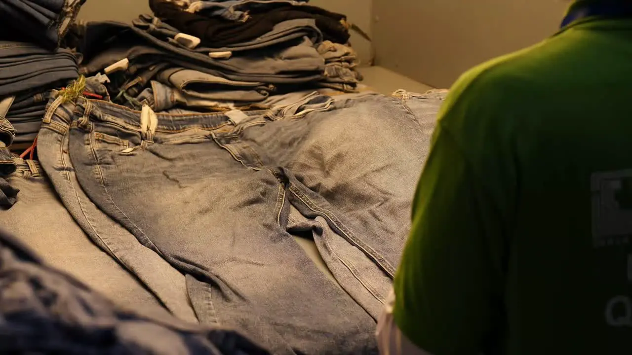 Worker Checking Stack Of Denim Jeans Under Light In Factory In Pakistan