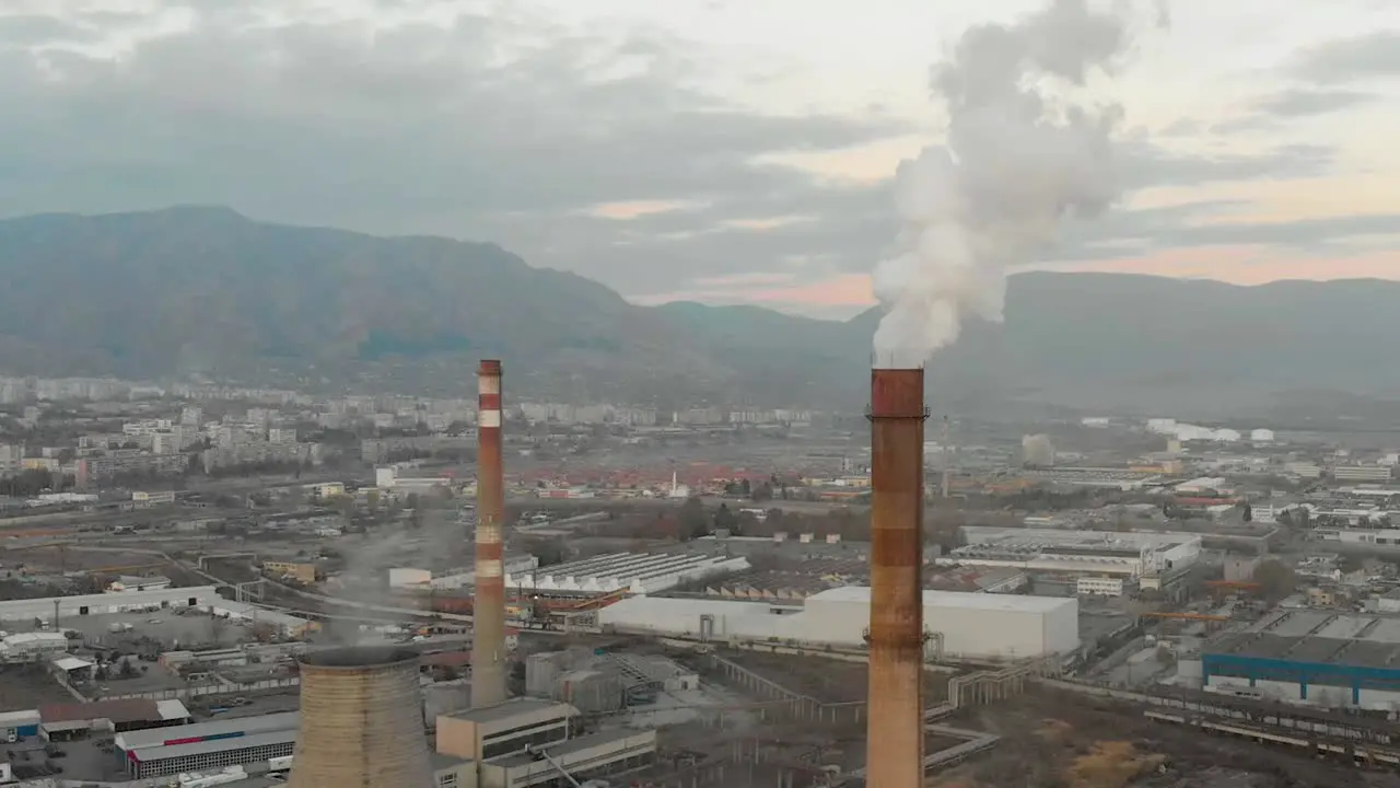 Industrial chimney smoking buildings and mountains as background aerial shot