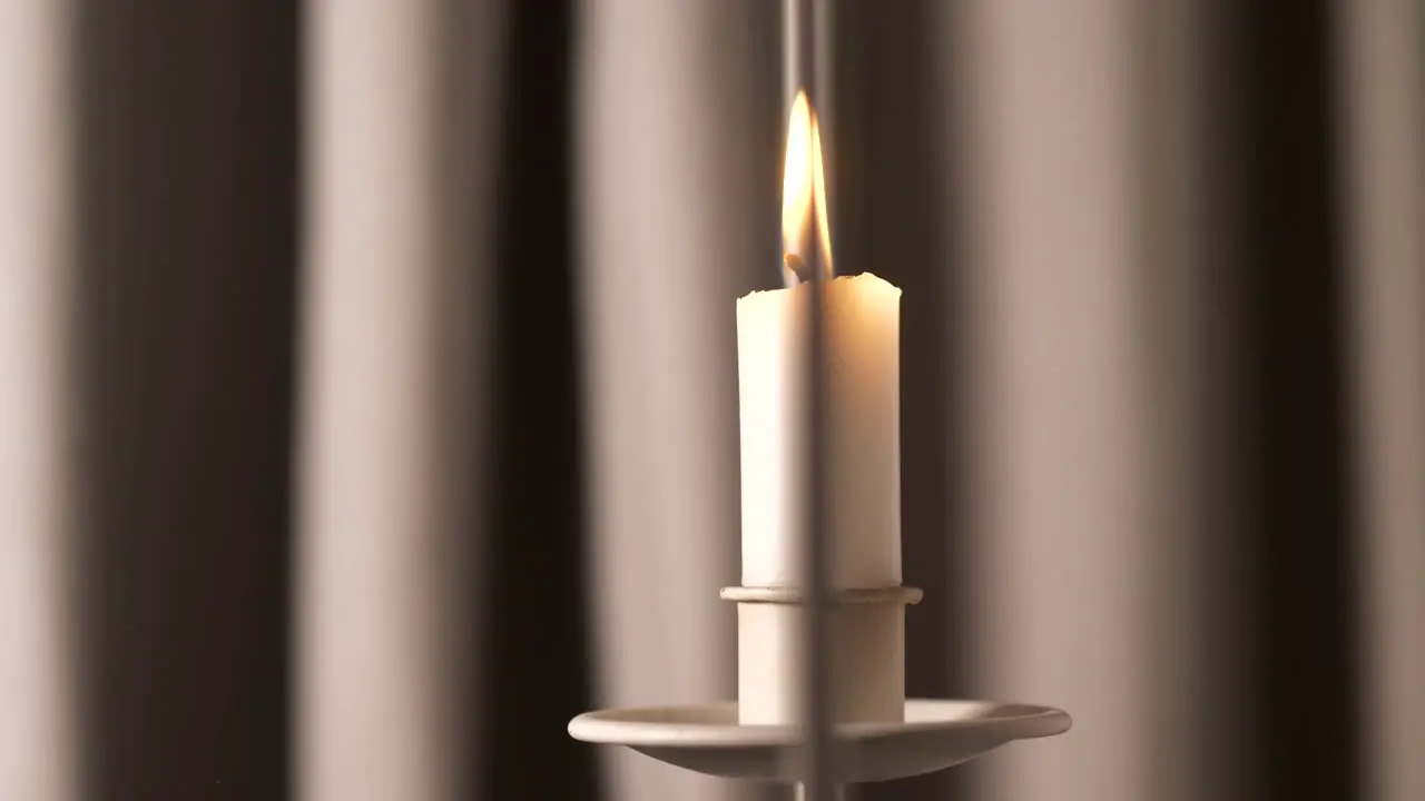 Soft candle burns in front of drapes close up bokeh slider shot