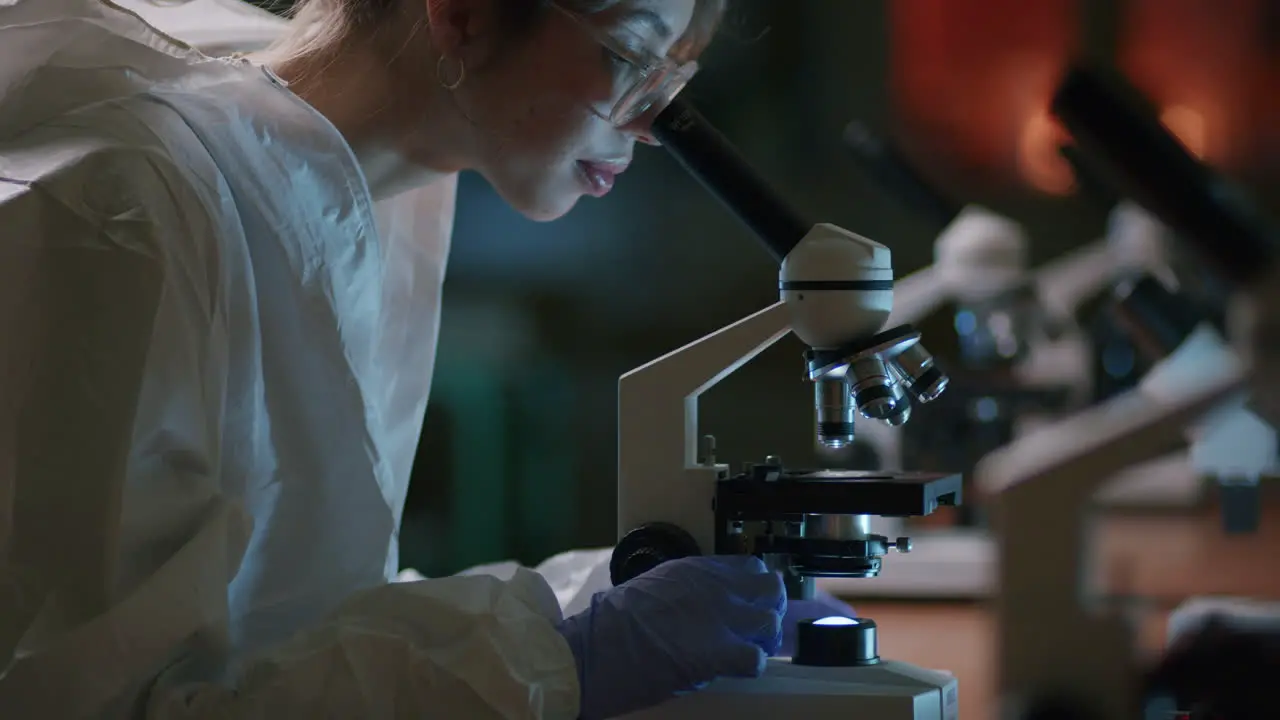 A young female scientist reviews a sample with the professional microscope in the laboratory—a medium tilt-up shot