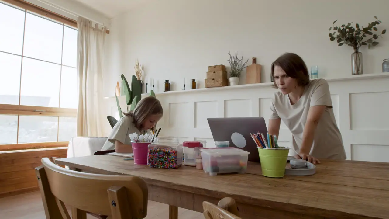 A Mother Gives Her Blonde Daughter Pencils So She Can Draw While She Gets Ready To Work From Home On Her Laptop