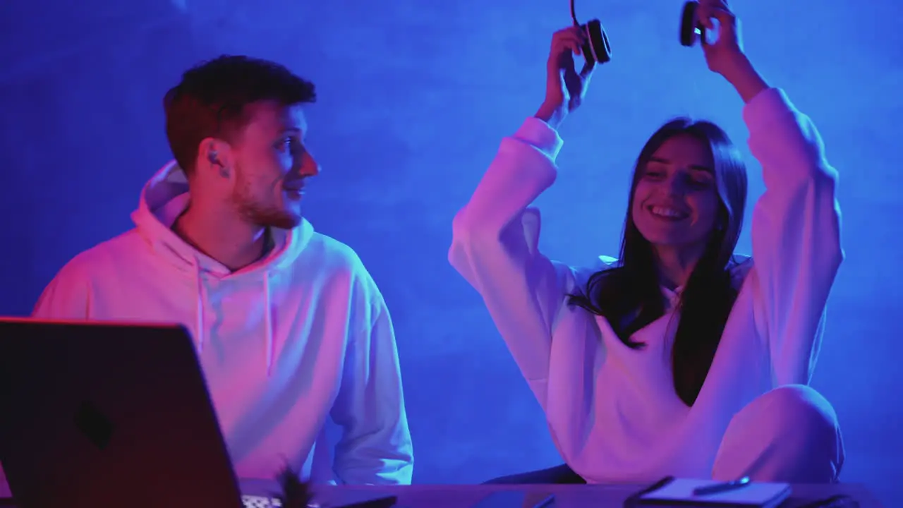 Modern Man And Woman Using A Computer And Wireless Headphones On A Neon Light Colorful Background