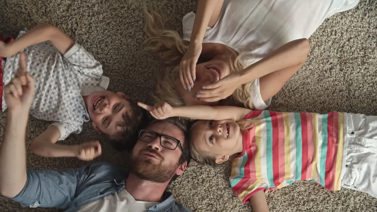 Top View Of Father And Mother And Two Children Lying On The Floor With Their Heads Together And Playing With The Index Finger