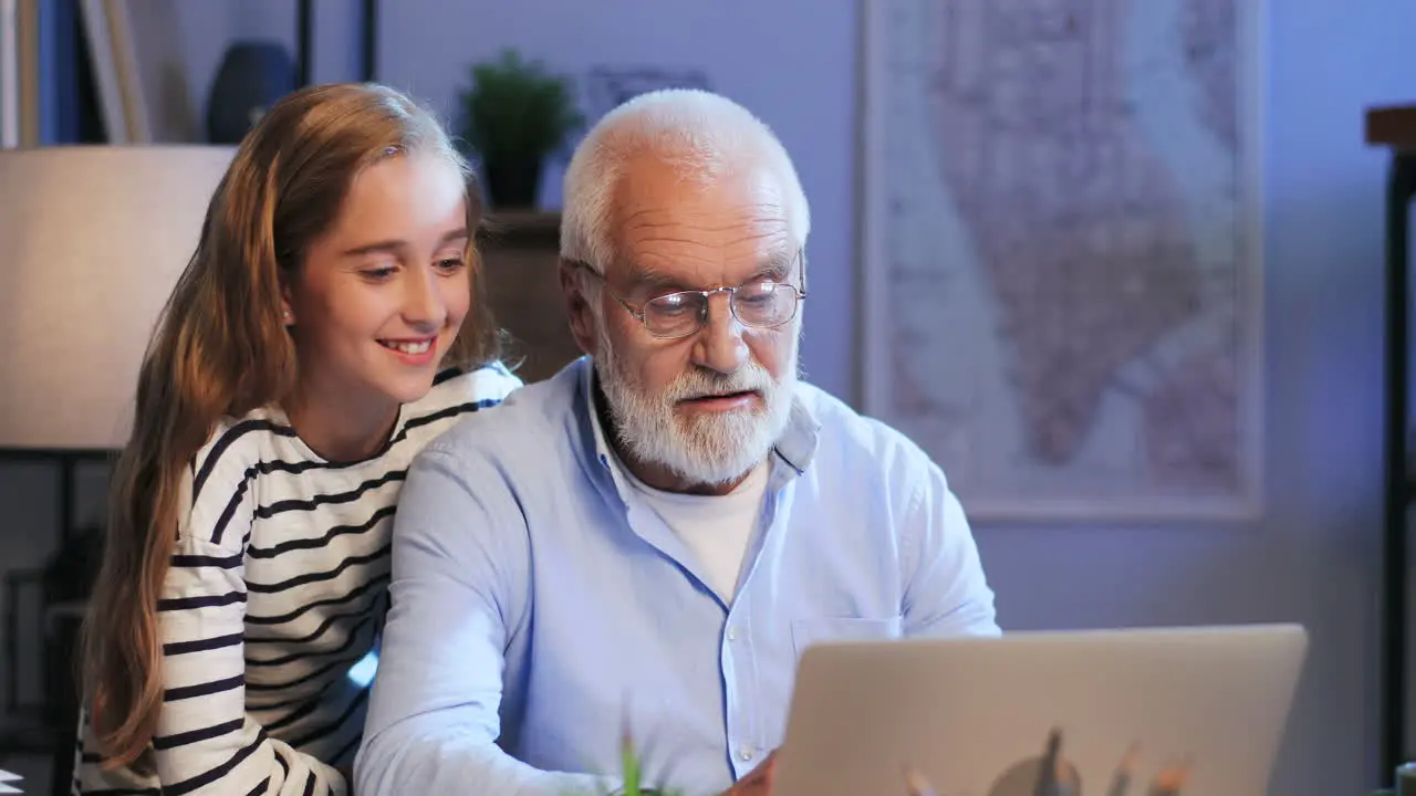 Smiled Grandfather And Granddaughter Sitting Being In The Cabinet At Home And Having A Videochat On The Laptop Computer Late At Night