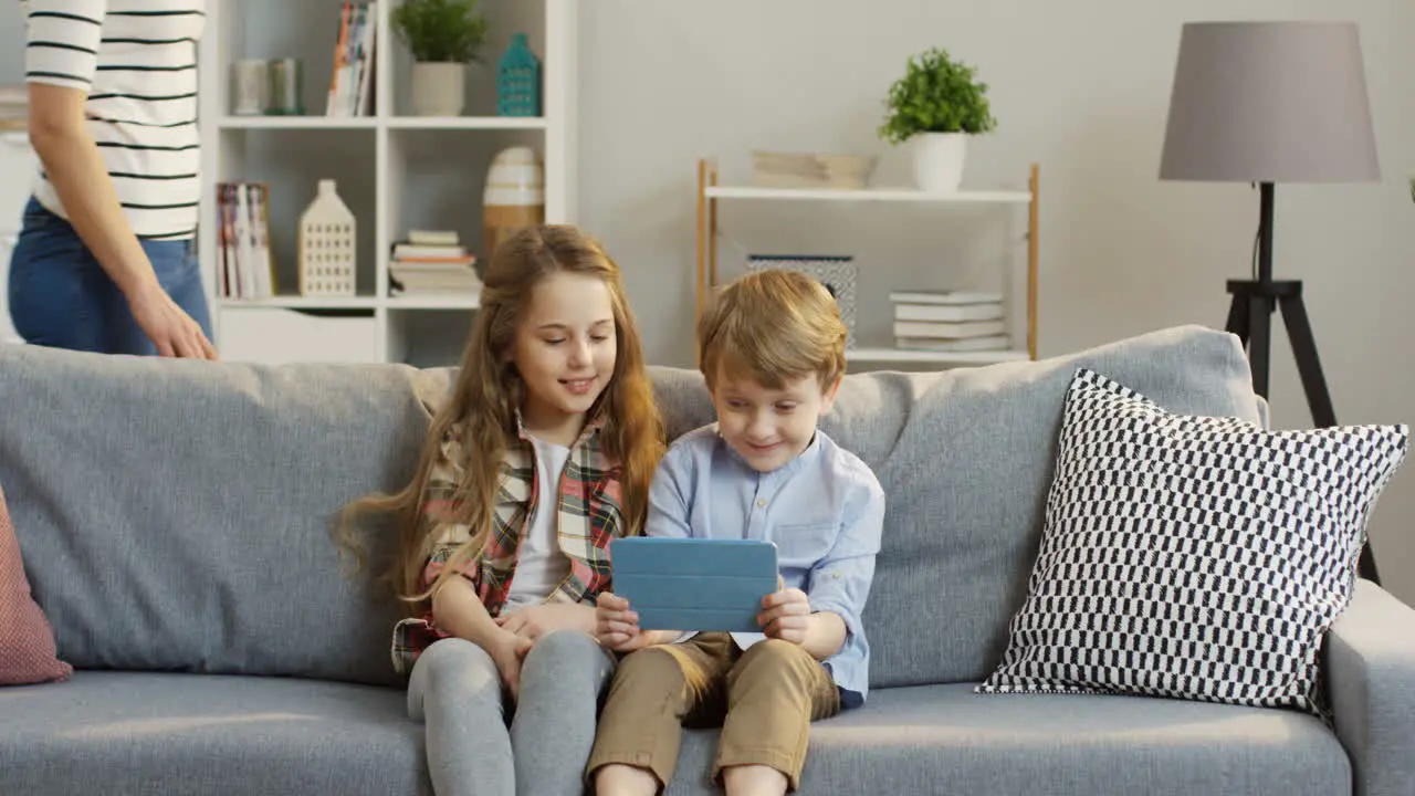 Cute Little Kids Sitting On The Couch And Watching Something On The Tablet Computer Then Their Mother Coming And Hugging Them