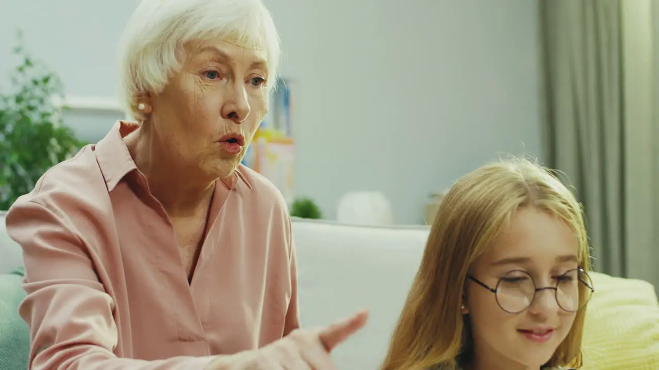 Portrait Shot Of The Pretty Teenage Girl In Glasses Doing Something On The Laptop Computer And Her Grandmother Talking And Telling Her What To Do While Looking At The Screen