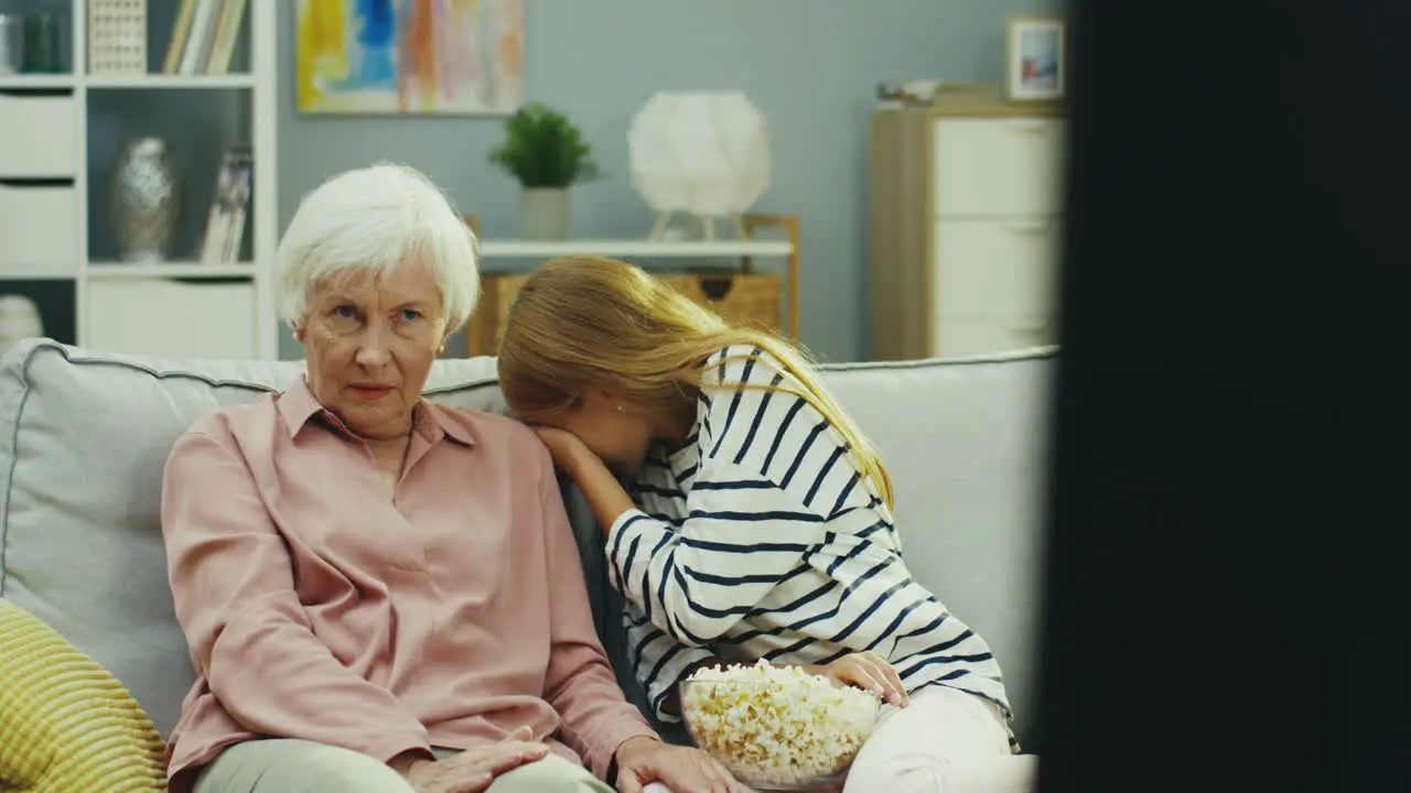 Cute Little Teen Girl And Her Grandmother Sitting On The Sofa At Home And Watching Something Scary On Tv Then Granddaughter Hiding Her Eyes And Being Afraid