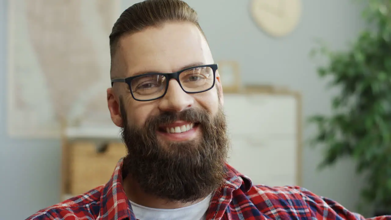 Portrait Of The Serious Young Man With A Beard And In The Glasses Looking Straight To The Camera And Then Smiling