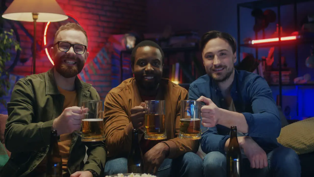 Portrait Shot Of The Three Mixed Races Young Handsome Guys Friends Smiling To The Camera With Beer In Hands In The Dark Living Room