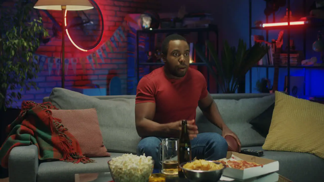 Young Man Eating Pizza And Watching American Football On Tv In The Dark Room At Night