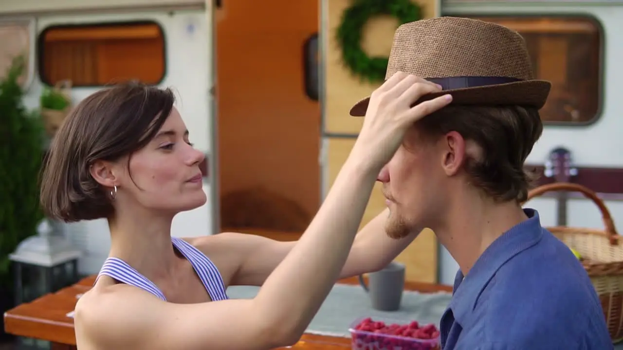 Cute Couple Man And Woman Having Fun Together At Wooden Table Outdoors Girl Putting Her Hat On A Man's Head