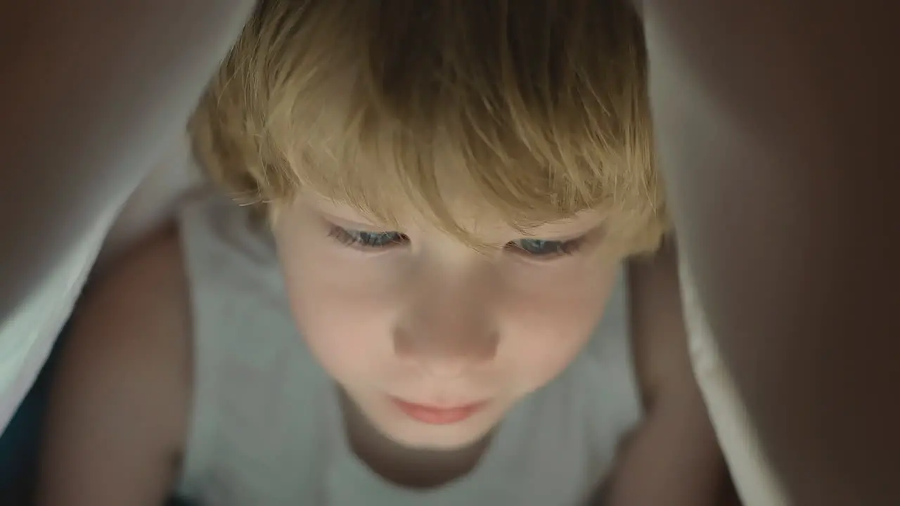 Little Boy Using A Tablet Covered By The Bed Sheet At Night