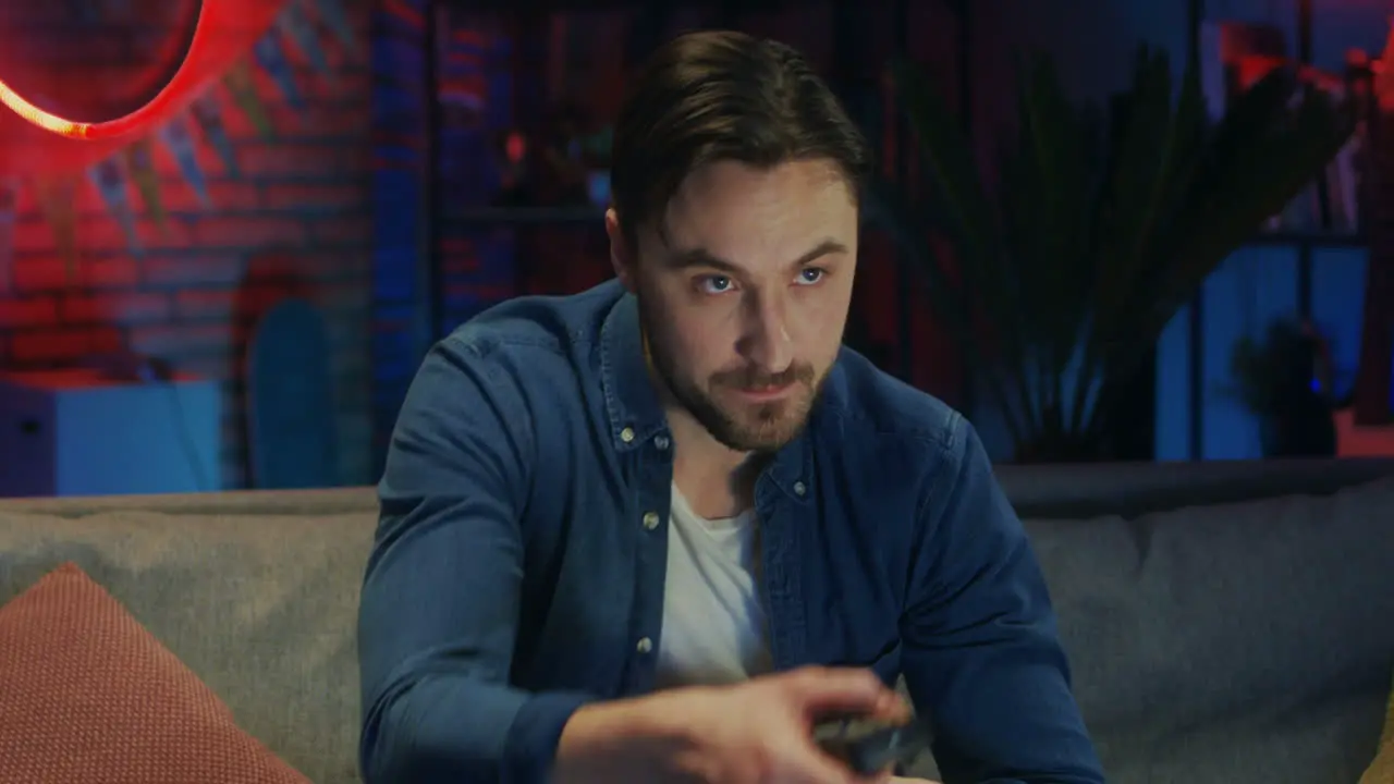 Portrait Shot Of The Good Looking Young Guy Sipping Beer From A Bottle And Watching Tv While Changing Channels In The Dark Living Room In The Evening