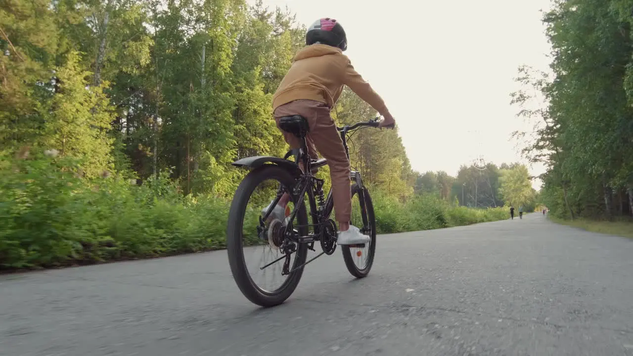 Rear View Of Kid Riding A Bike In Forest Path While Other People Are Running