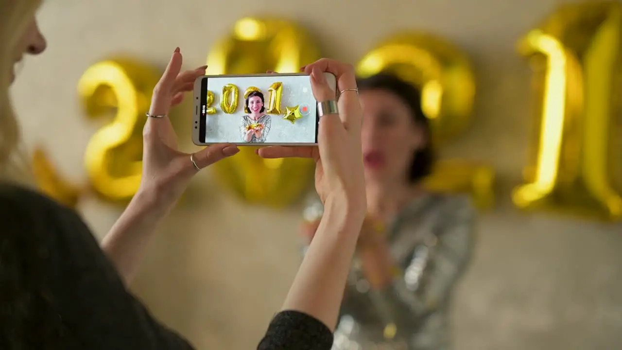 Close Up Of Hands Taking A Photo Of A Young Pretty Woman Blowing Gold Glitter Confetti And Wearing Evening Dress