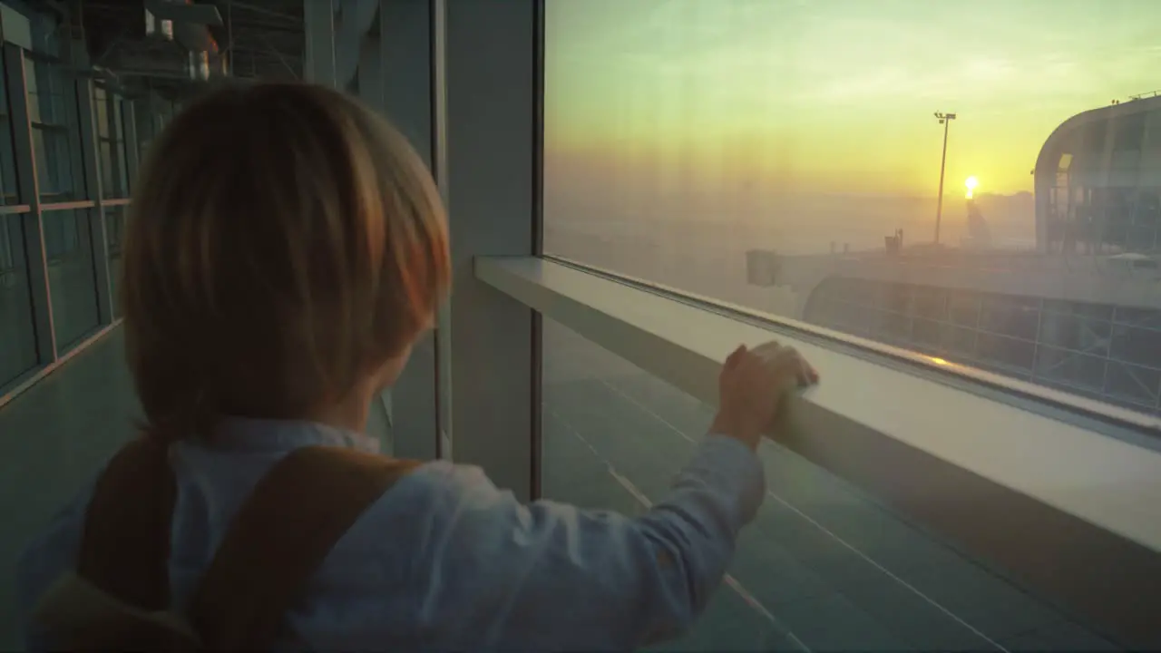 Close Up Of The Rear Of The Small Boy Standing At The Airport Window And Looking At The Beautiful Sunset