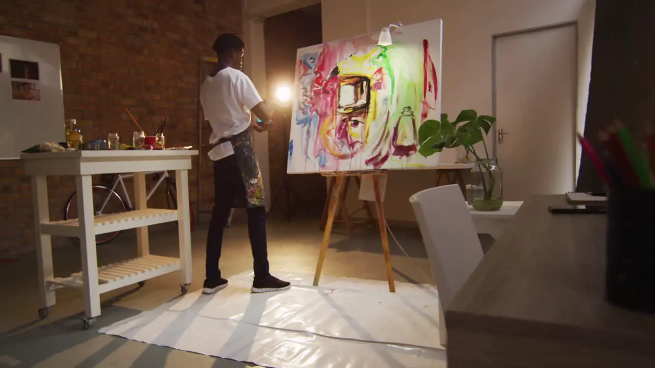 African american male artist wearing apron painting with palette knife on canvas at art studio