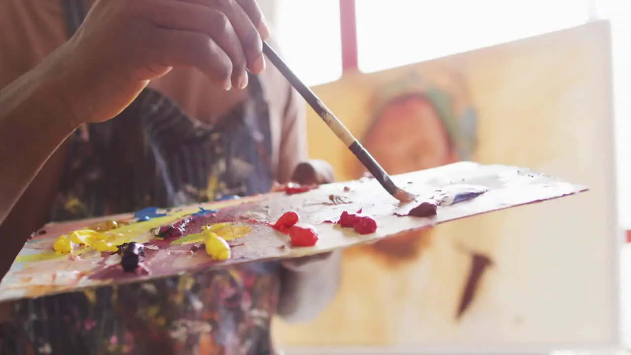 Mid section of male artist wearing apron mixing colors in a palette with a brush at art studio