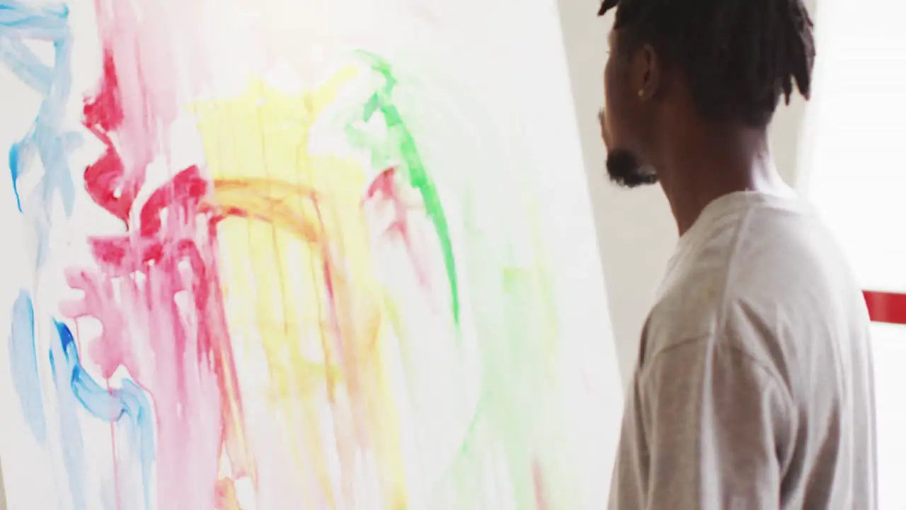 Thoughtful african american male artist sitting looking at his painting at art studio