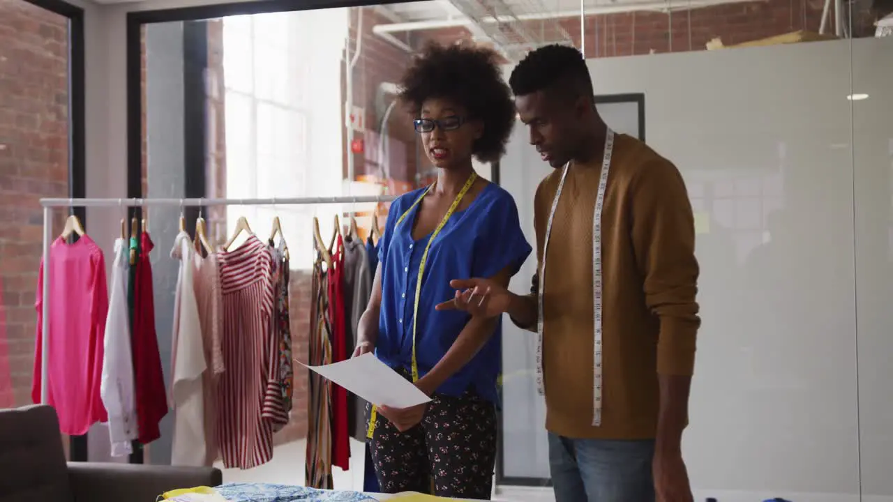 African american male and female fashion designers in discussion at work looking at document